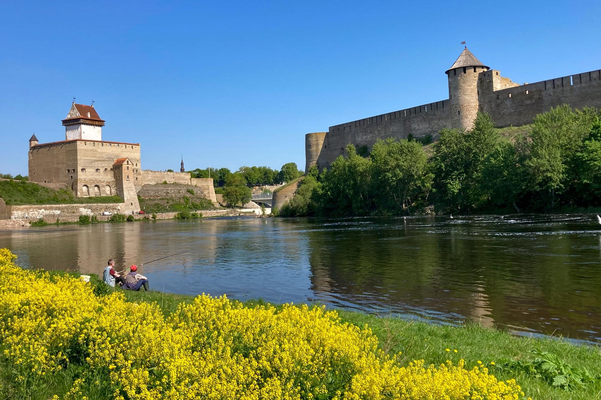 Men are seen fishing near the fortresses of Narva, left, and Ivangorod, Russia, right, in Narva, Estonia, on Wednesday, May 24, 2023. 