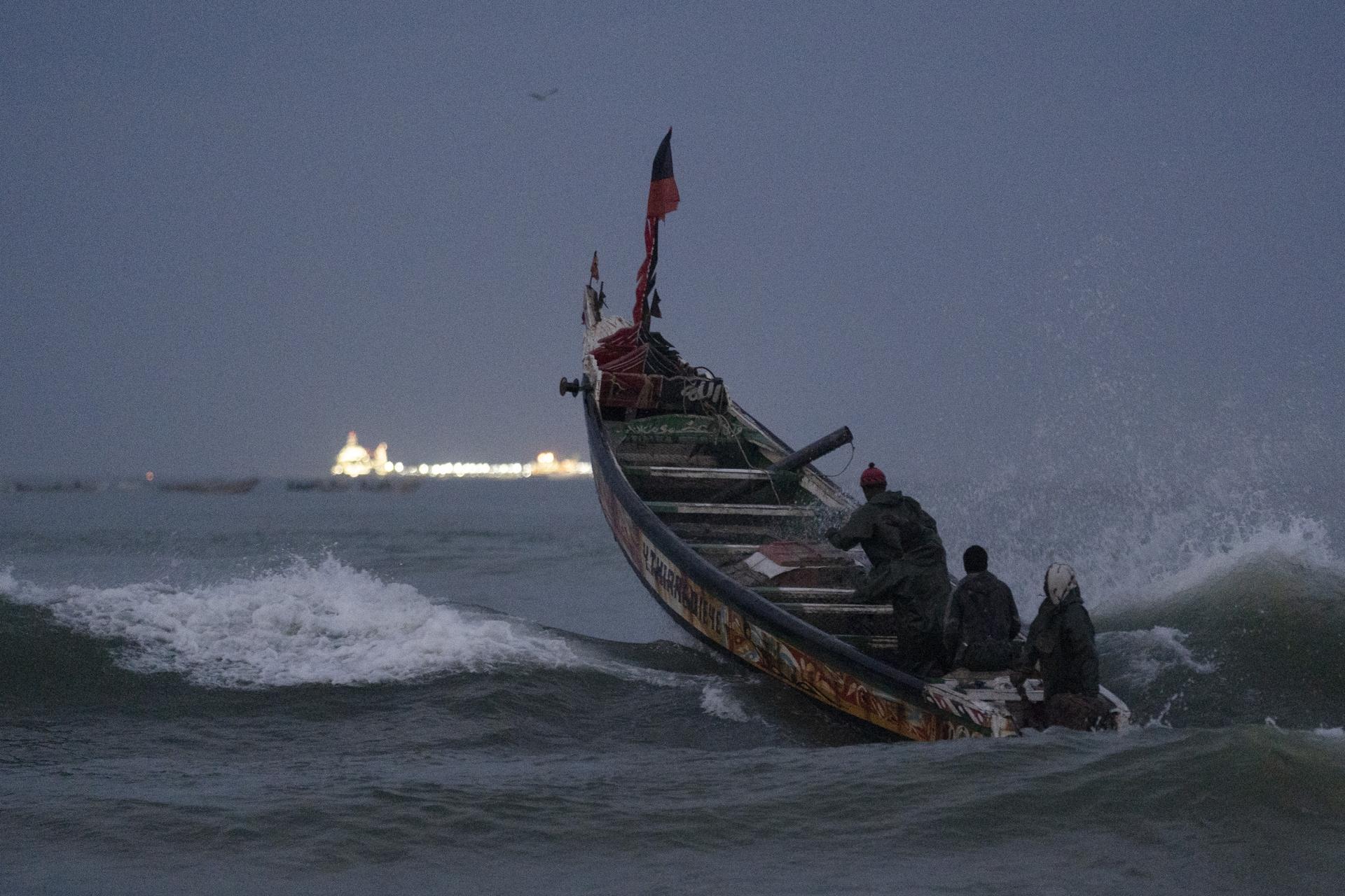 Fishermen on a traditional boat known as pirogue leap over a wave heading out to the Atlantic Ocean as an offshore gas terminal is seen at the horizon in Saint-Louis, Senegal, Jan. 18, 2023.