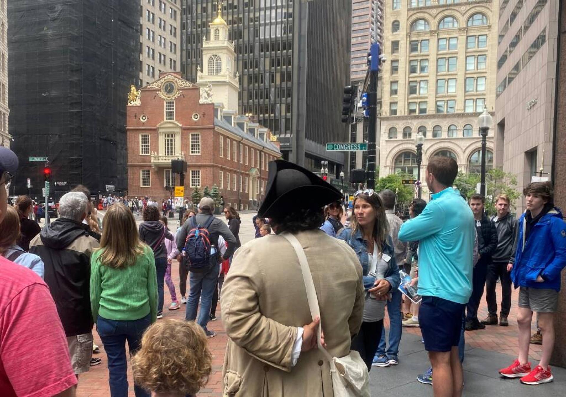 A Freedom Trail guide discusses the history of the Old State House with a tour group in downtown Boston.