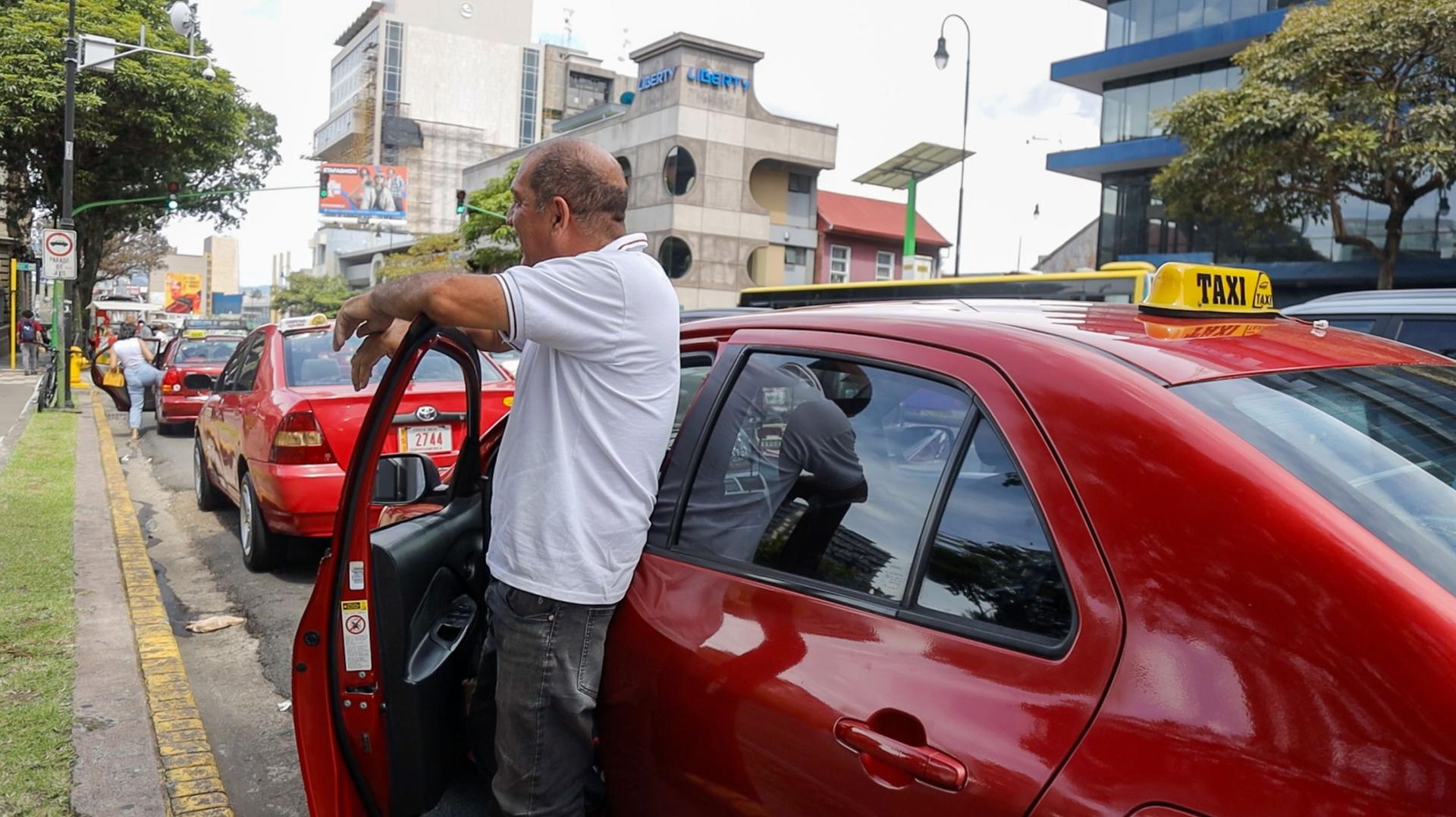 Taxi driver Mauricio Segura stands near a red car. 