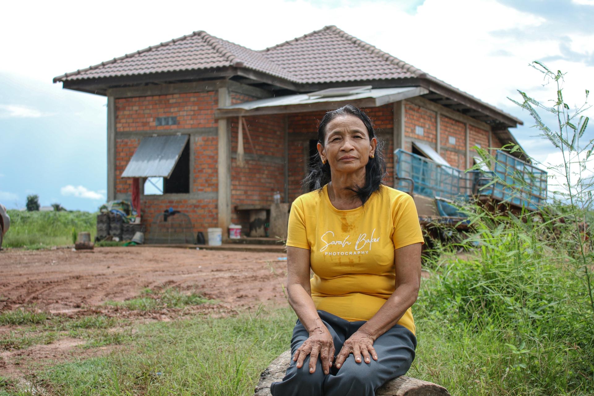A woman posing in a yellow shirt and jeans in front of a house