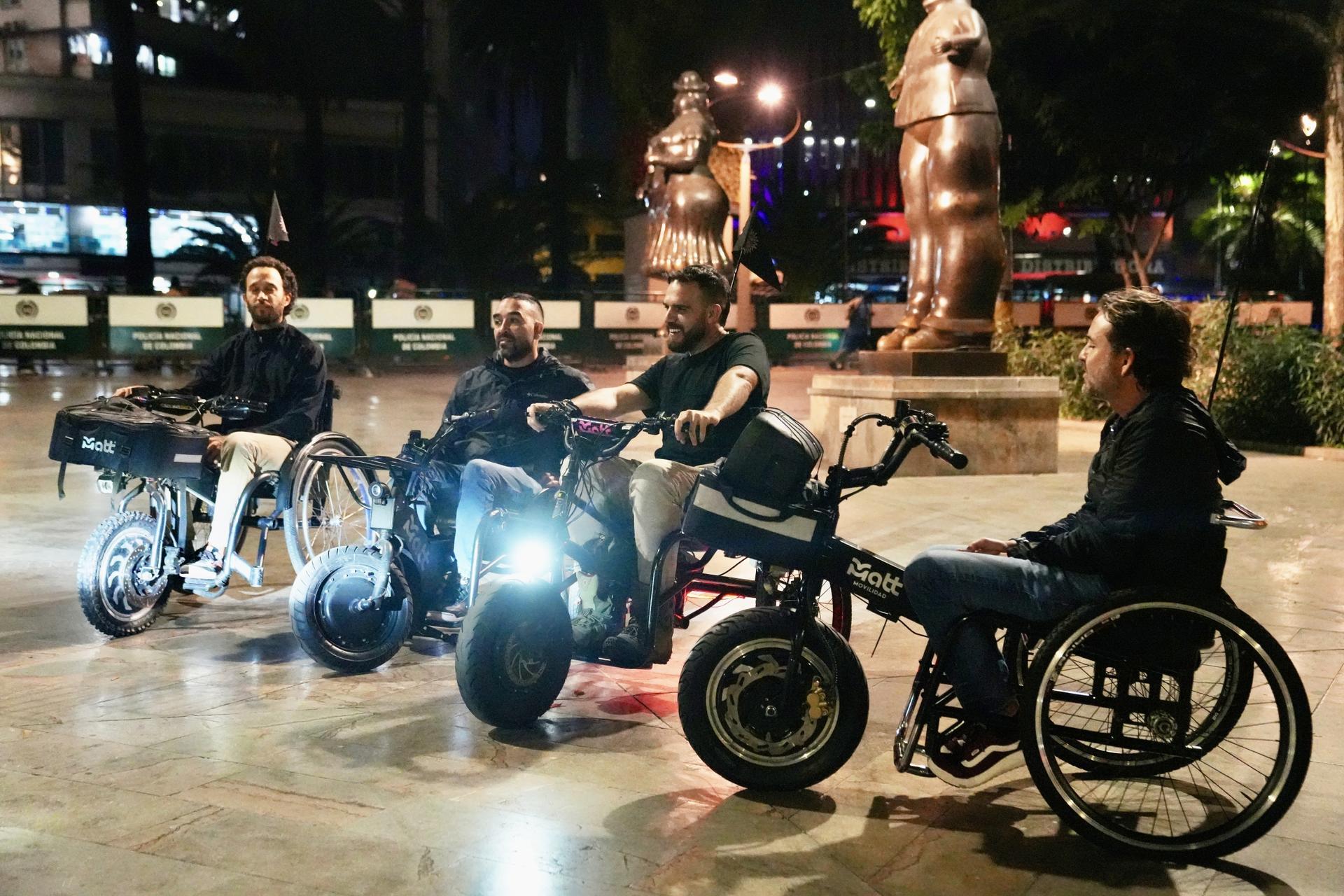A group of people sitting on electric wheelchairs at night