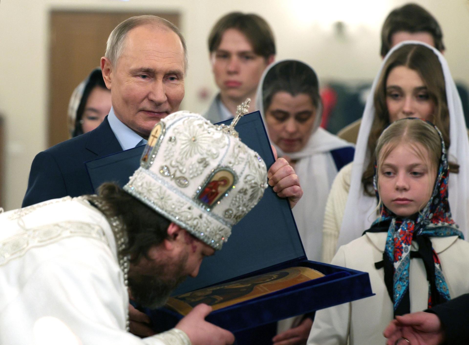 Russian Orthodox Archbishop of Odintsovo and Krasnogorsk Foma (Nikolay Mosolov), foreground, kisses an icon as Russian President Vladimir Putin, left, stands near after attending an Orthodox Christmas service.