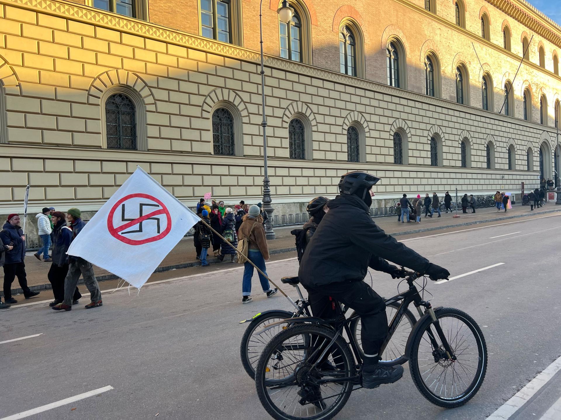 A protester in Munich rides a bicycle carrying a sign with the Nazi symbol crossed out on a white flag. 