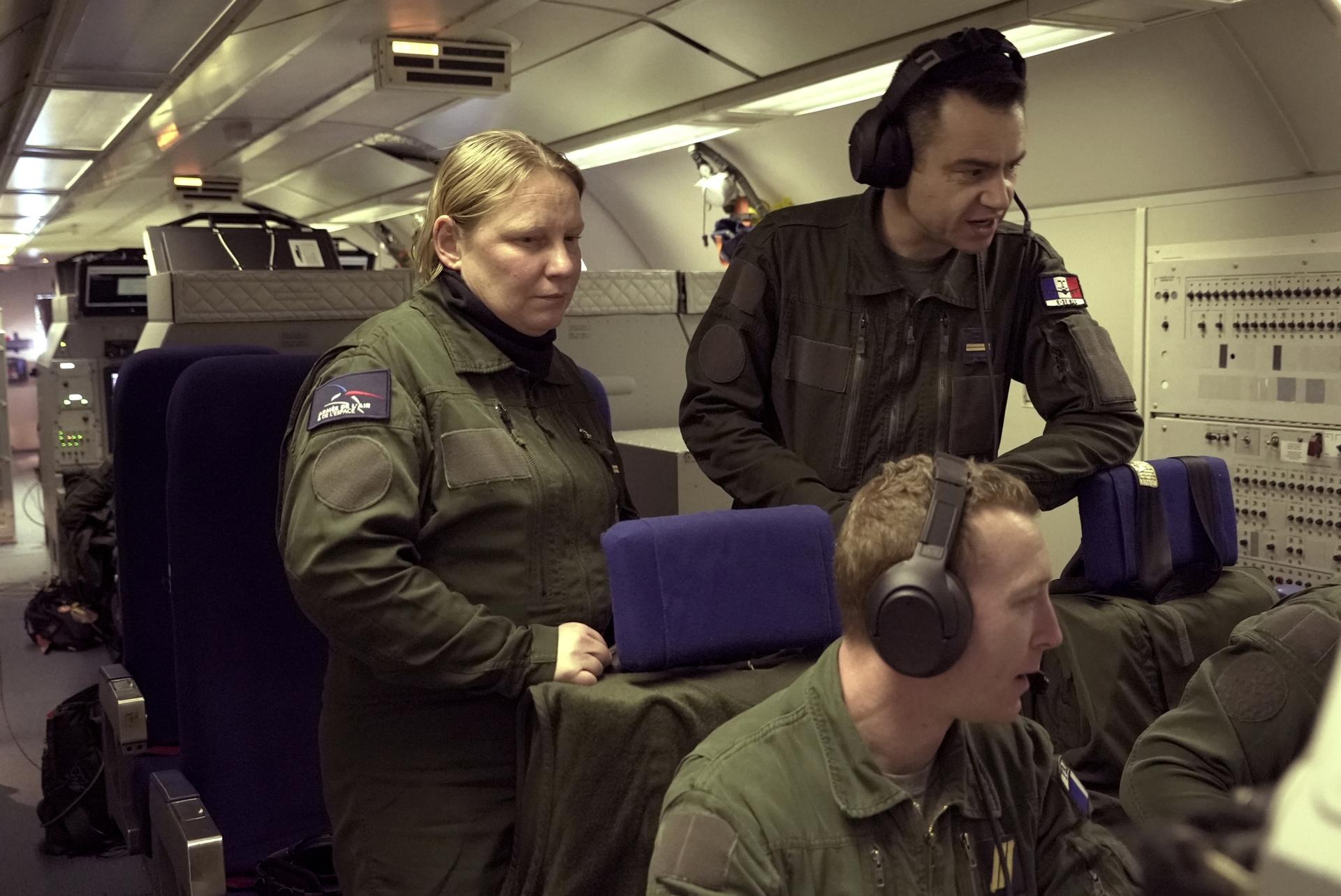 three military personnel on a plane reviewing a monitor