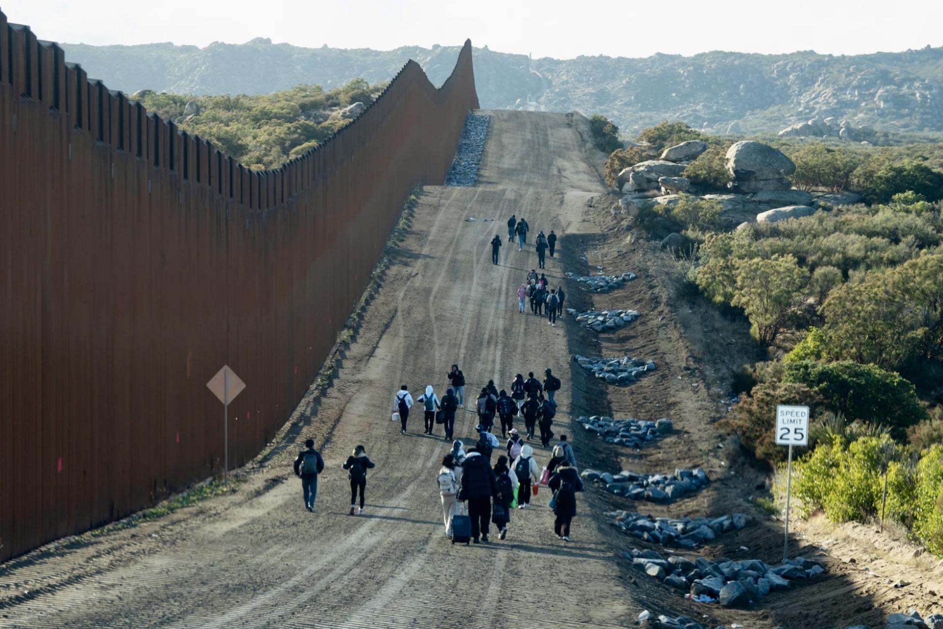 Migrants walk west along the border wall on the U.S. side.