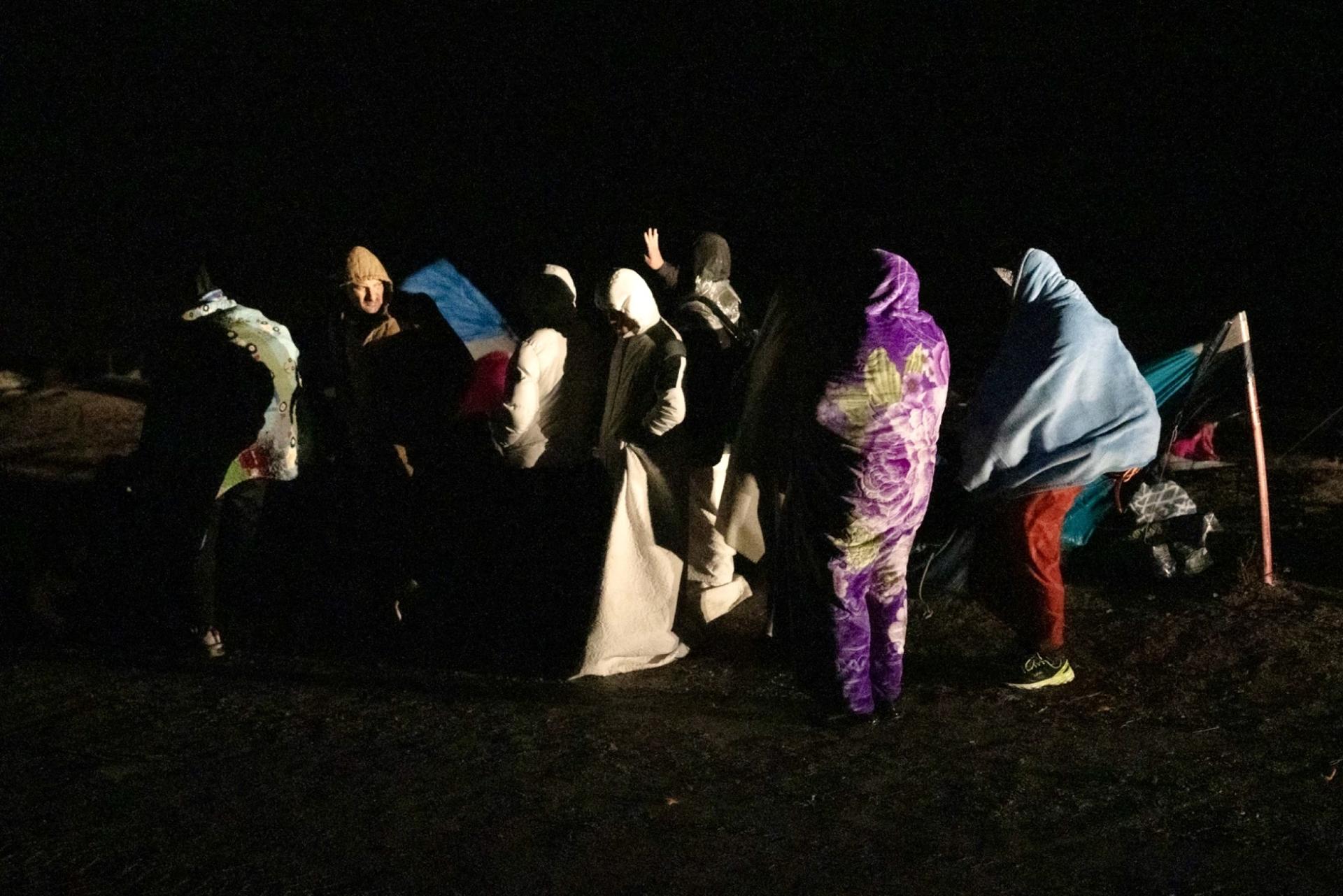 Migrants wrap themselves in damp blankets and shiver in the cold and rain