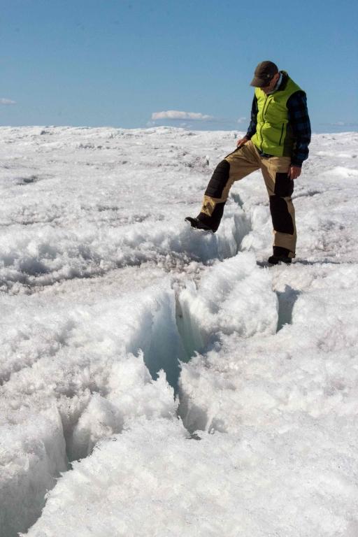 A man in a fluorescent vest steps over a large crack in the ice sheet.