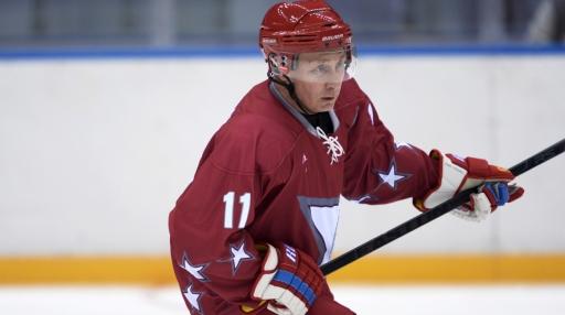 Vladimir Putin holds a hockey stick dressing in a red and white hockey uniform and helmet.