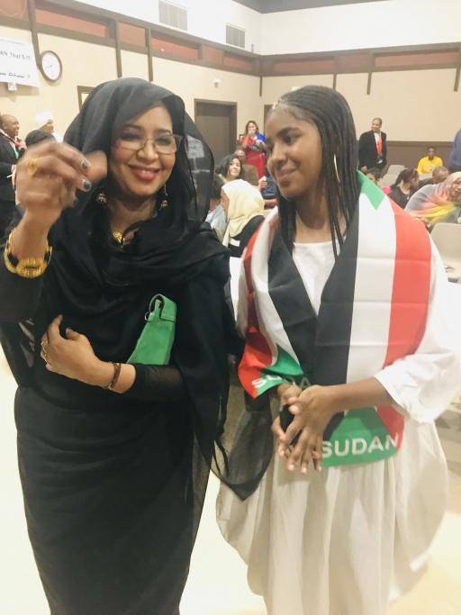 Girl dances with her mom wearing scarf with Sudan flag colors. 