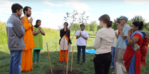 People stand before tree seedling with hands folded in prayer