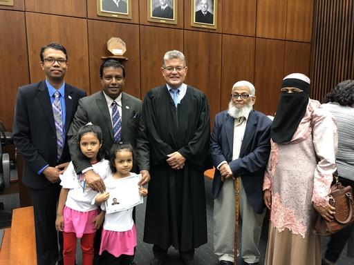 A man stands alongside a judge and his family at his naturalization ceremony.