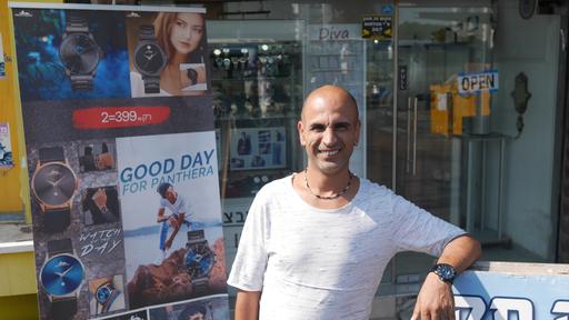 A man in a light T-shirt poses in front of a shop