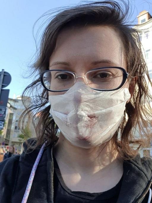 A woman with glasses wears a sweatshirt and a white face mask. 
