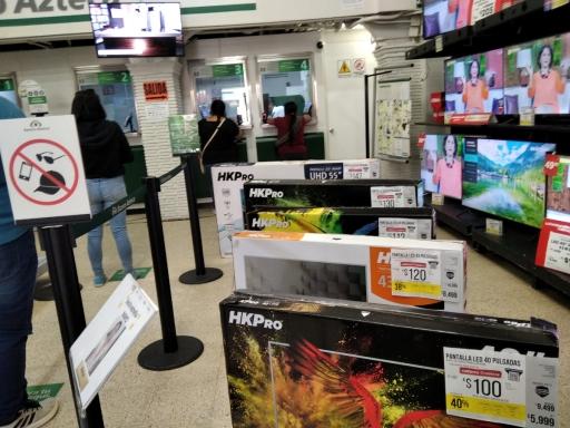 A line at a bank next to TVs for sale in the same space 