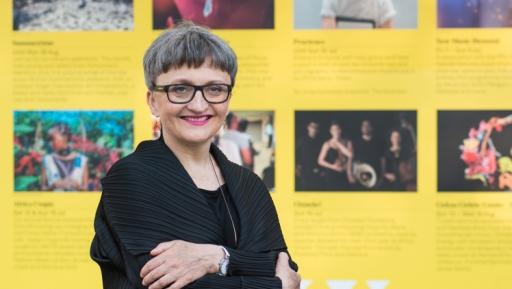 A white woman wearing glasses and a short hair cut smiles in front of yellow backdrop 