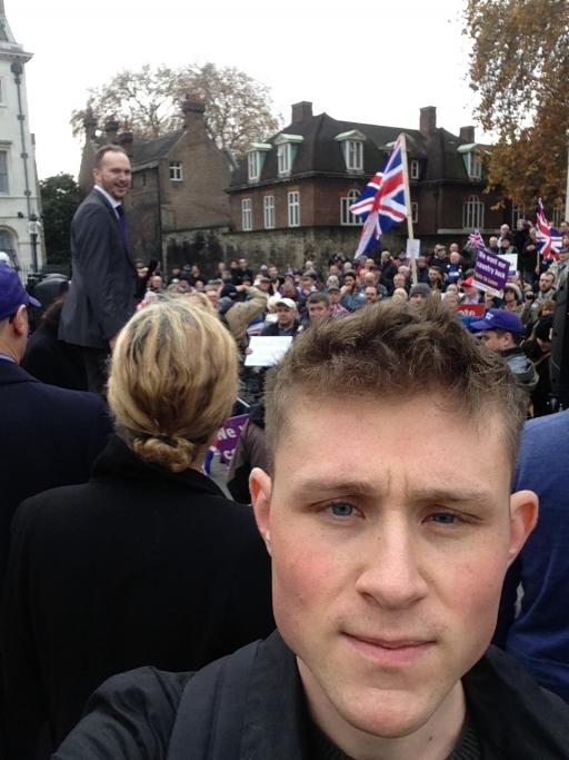 A white man with blond hair takes a selfie at a rally