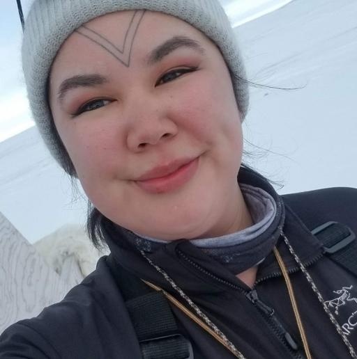 A woman with a facial tattoo on her forehead wears a hat and smiles in this selfie