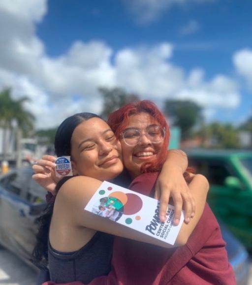 Two young people embrace each other and show an "I voted" sticker 