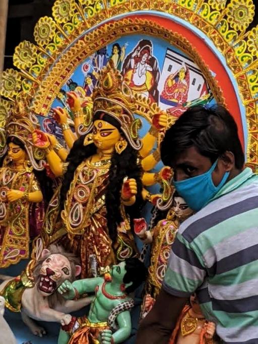A man holds an ornate Durga idol in his arms while he wears a mask