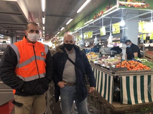 A man wearing an orange vest stands near his older friend at an indoor market