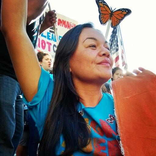 A woman wearing a blue shirt stands with a hand up and a monarch butterfly image near her. 