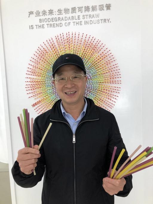 A Chinese man holds straws in both of his hands and smiles