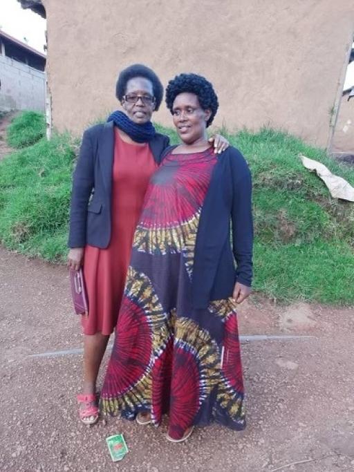 Two women pose together in Rwanda for a photo wearing reddish traditional clothing.