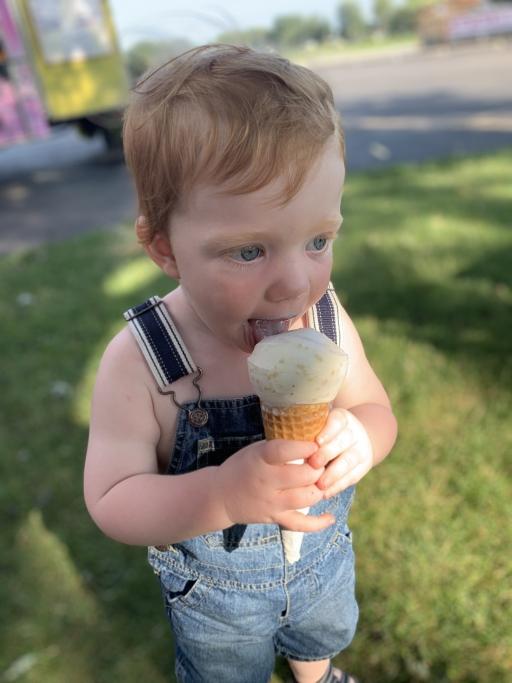 A small toddler eats an ice cream cone in overalls