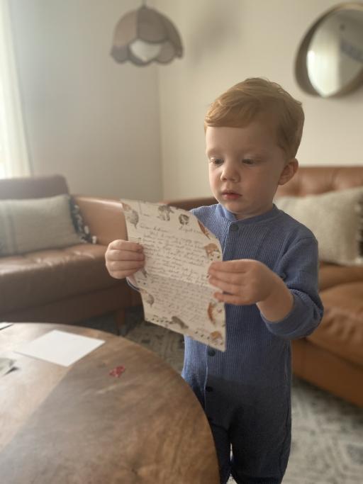A toddler holds a letter in his hands and reads it