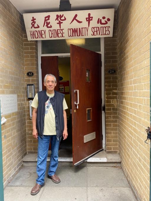 A man stands in front of a door with the words 'Hackney Chinese Community Services' written above in Chinese and English.
