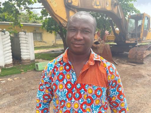 Solomon Noi is the head of waste management in Accra, wearing a brightly colored top near heavy machinery. 