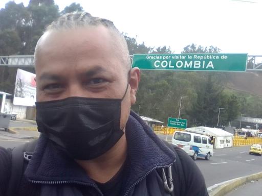 Jose Loya takes a selfie while wearing a black face mask in front of a green sign that reads "Colombia." 