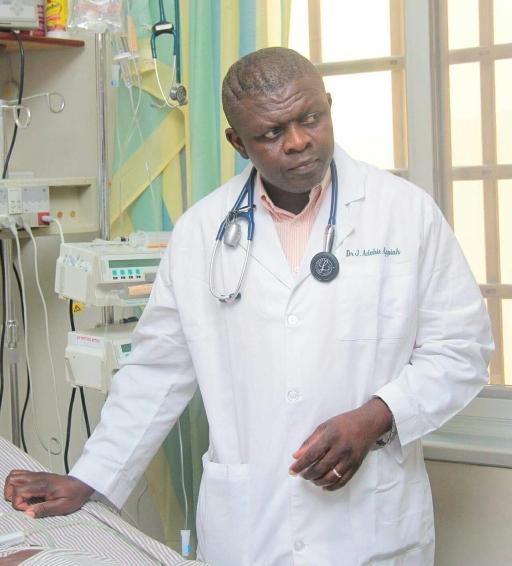 A Ghanaian doctor stands in a hospital room with wearing a white coat.