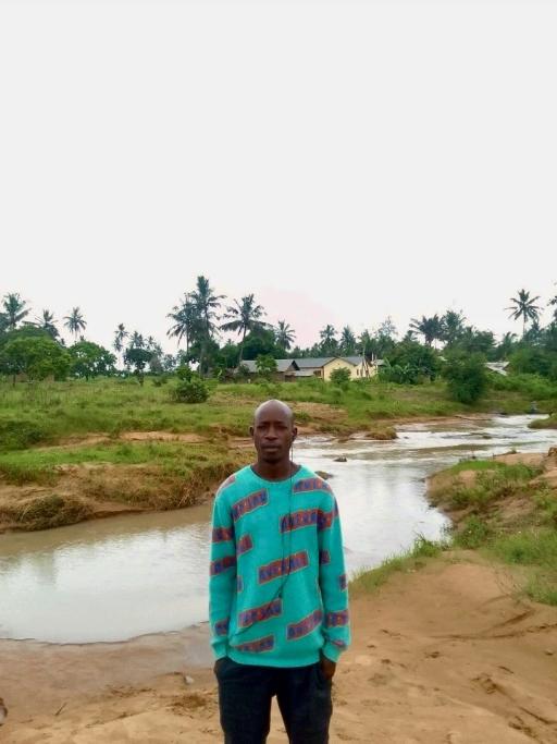 Photo of a Black male standing in front of a river and wearing a turquoise hoodie