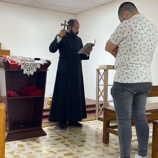 Father Qasha Shamoun (left), a priest at the Ancient Church of the East, leads a congregant in prayer, Baghdad, Iraq, Aug. 27, 2023.