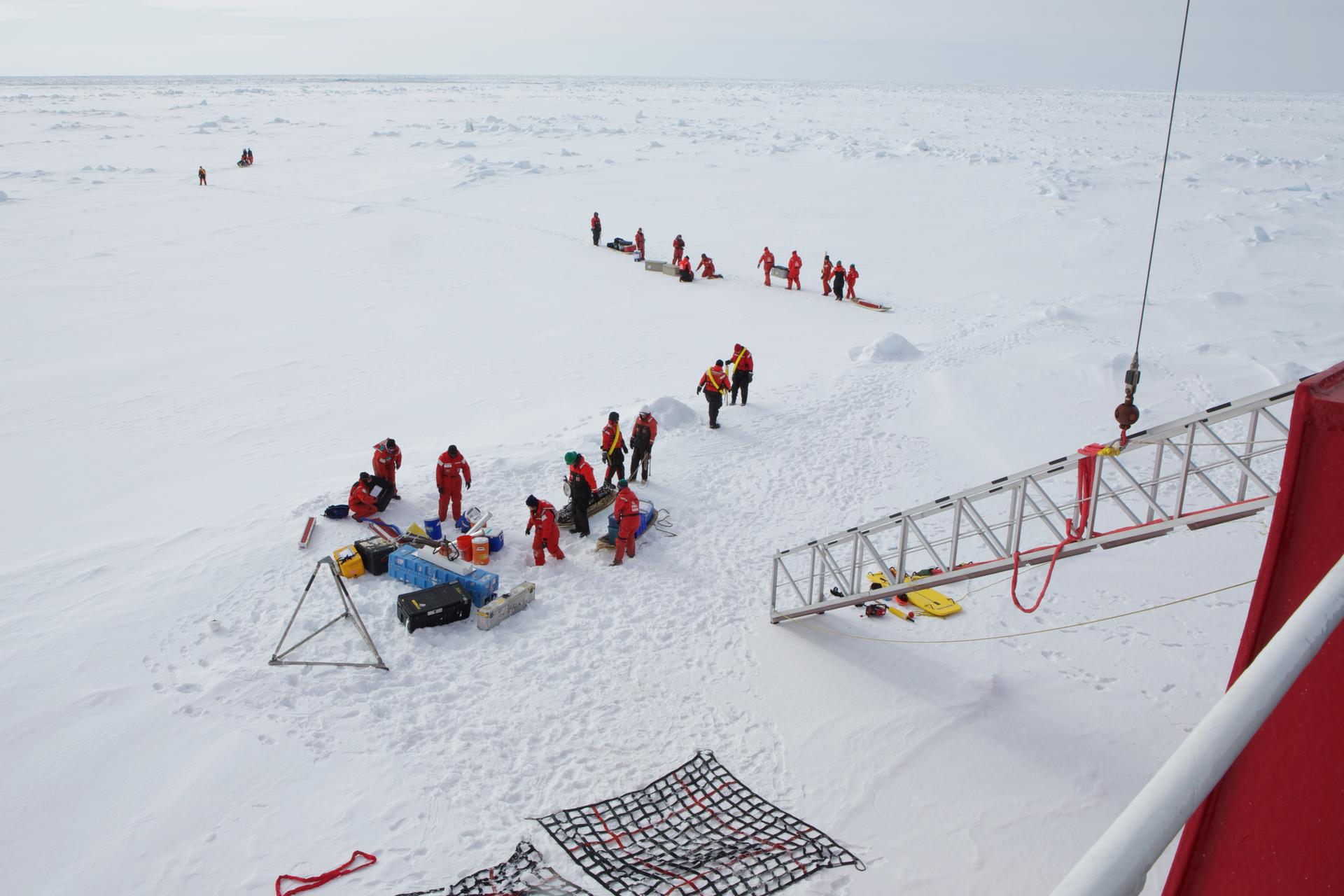 Crew and scientists traveling on the U.S. Coast Guard icebreaker Healy unload equipment in the lee of the parked ship before hiking off to set up their research projects in undisturbed snow.