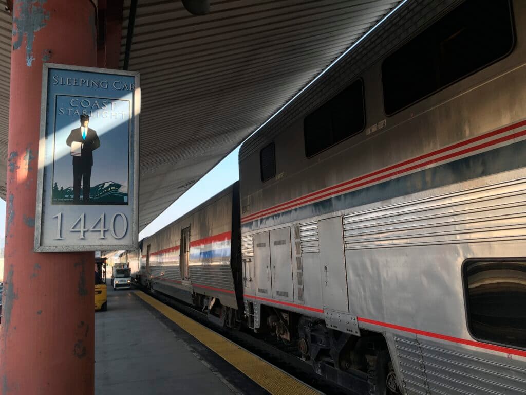 A train platform with a sign reading "Sleeping Car Coast Starlight 1440" next to a silver-colored Amtrak train with red and blue stripes.