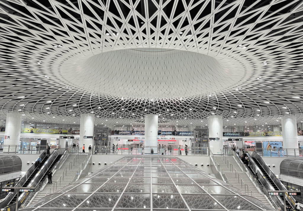 Interior of a large, modern transportation hub with a distinctive, patterned domed ceiling, multiple escalators, and visible signage.