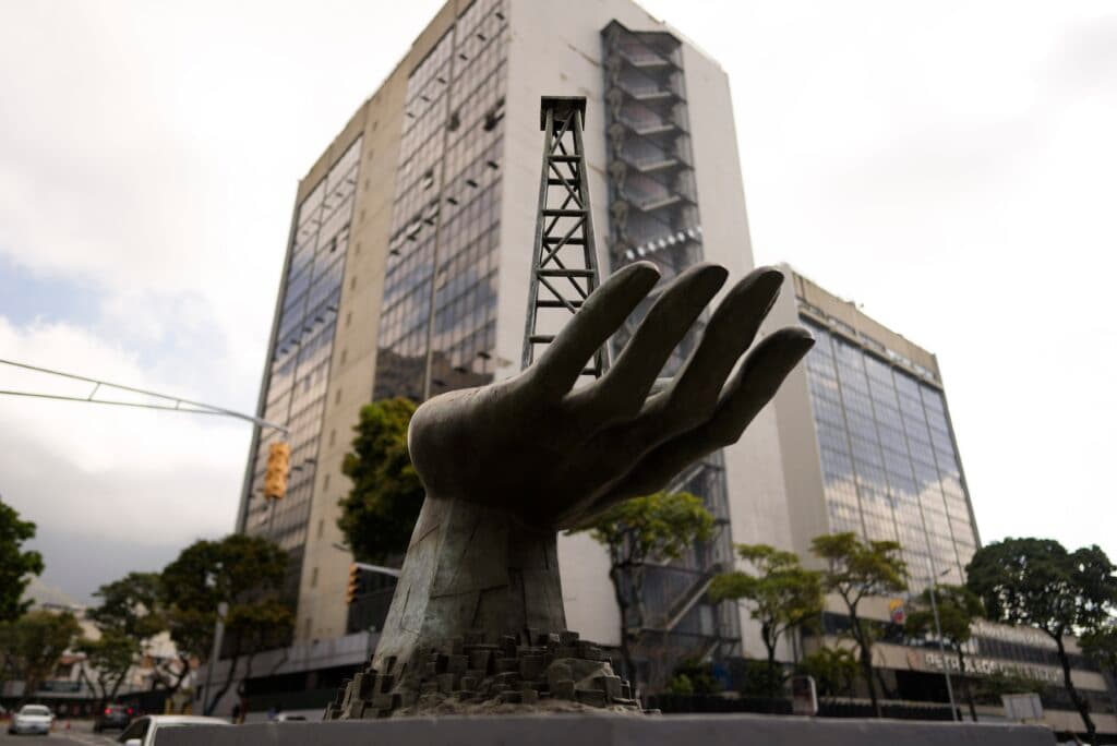 A sculpture of a large hand holding an oil derrick, set against the backdrop of a modern office building with glass windows.