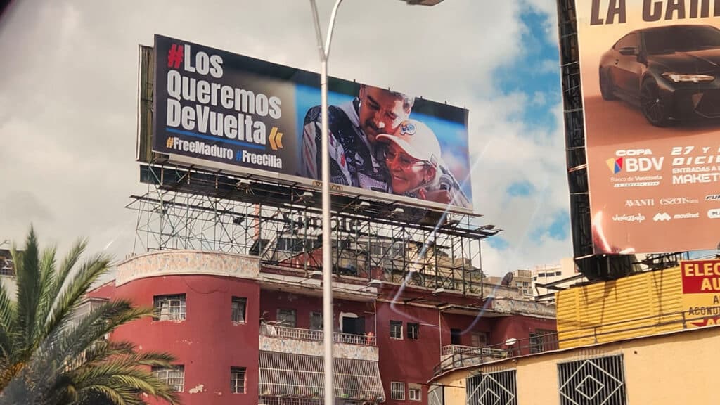 A billboard on top of a building features a hug between two people with the text "#Los Queremos De Vuelta #FreeMaduro #FreeCilia."