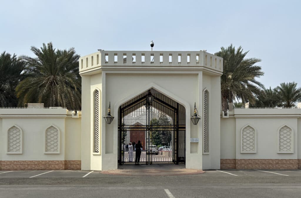 A large, ornate entrance gate with intricate patterns flanked by palm trees.