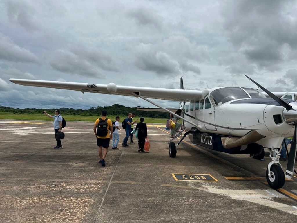 People boarding a small aircraft on an airport tarmac under a cloudy sky.