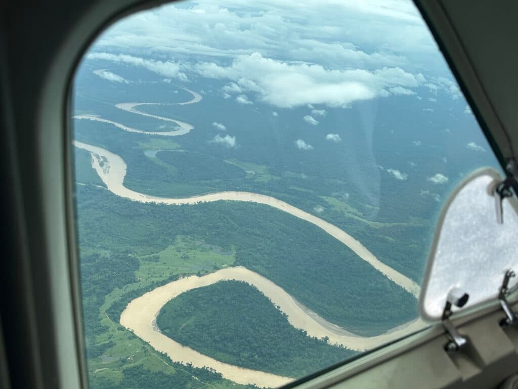 Aerial view of a winding river cutting through a dense green forest, as seen through an airplane window.
