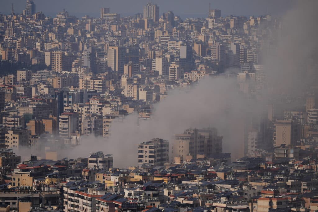 A cityscape with numerous high-rise buildings and a cloud of smoke rising between some of the structures.