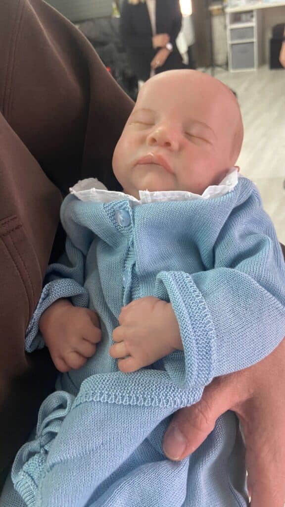 A sleeping baby is cradled in a person's arm, wearing a light blue knitted outfit.