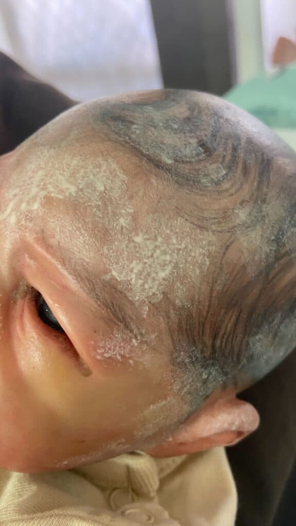 Close-up of a lifelike doll's head with painted hair and visible texture details.