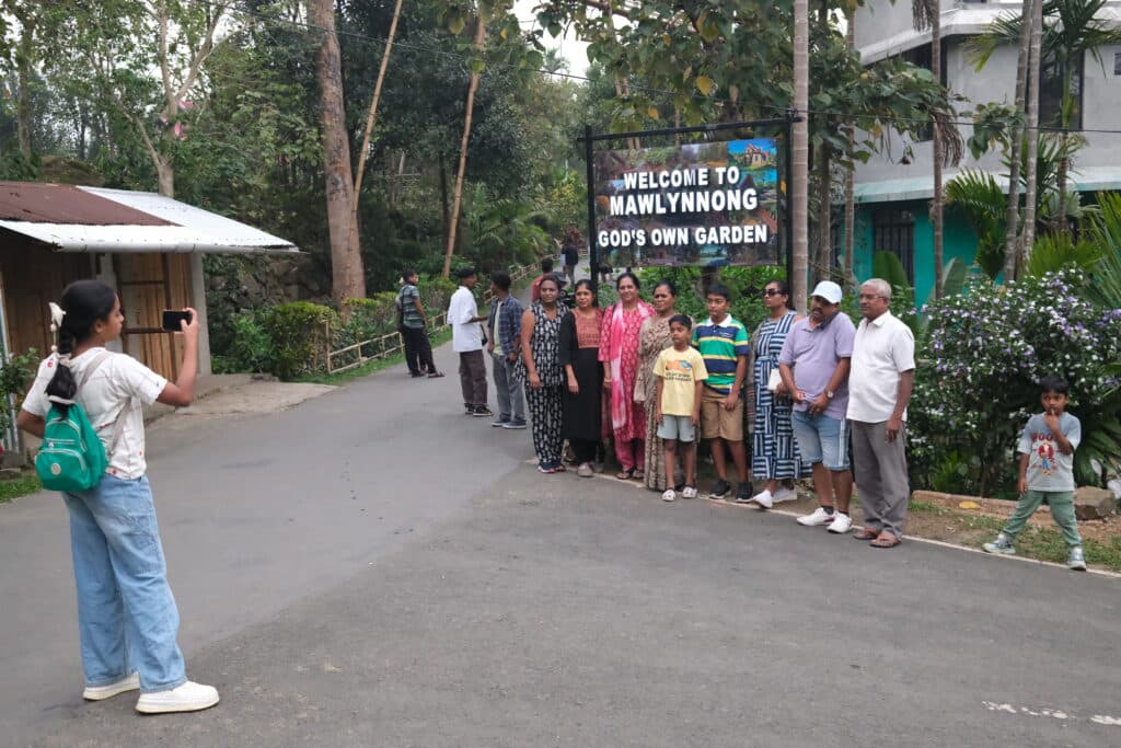 A group of people posing for a photo in front of a sign that reads "Welcome to Mawlynnong God's Own Garden."