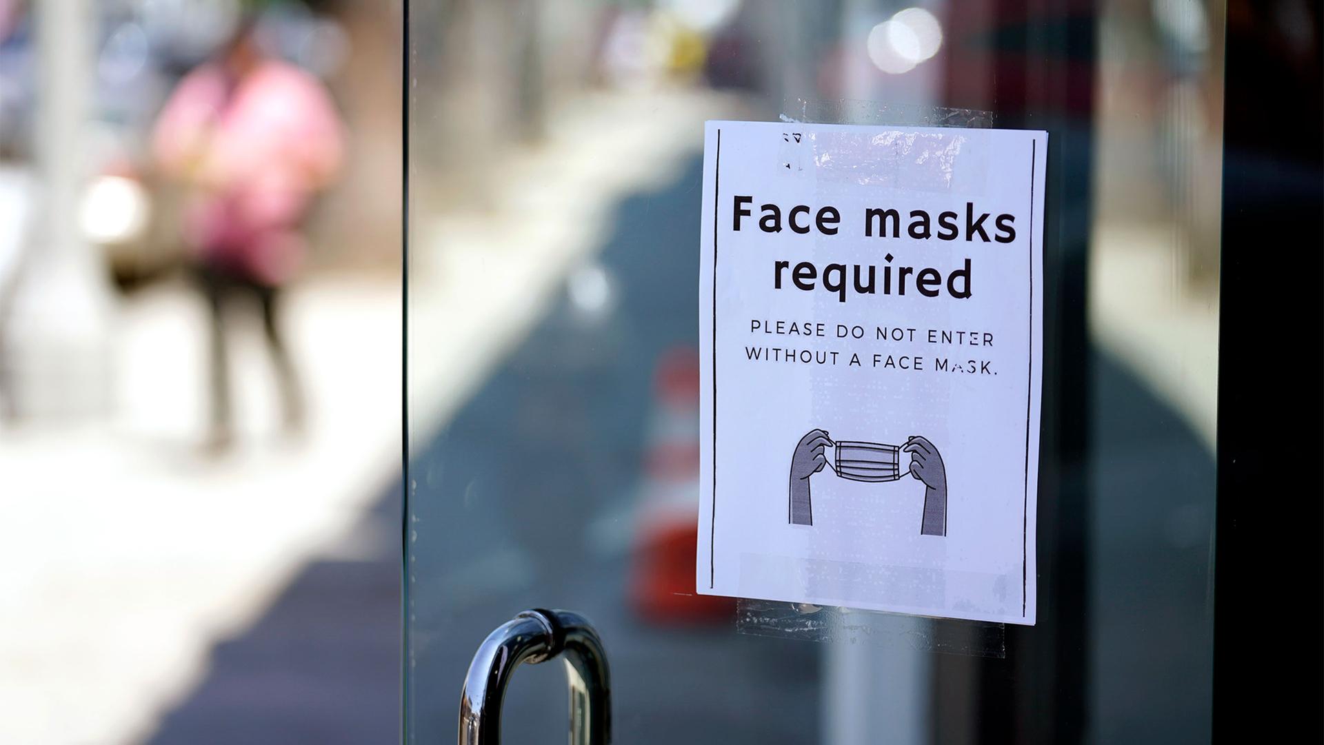 Door with a "face masks required" sign and a person blurred in the distance