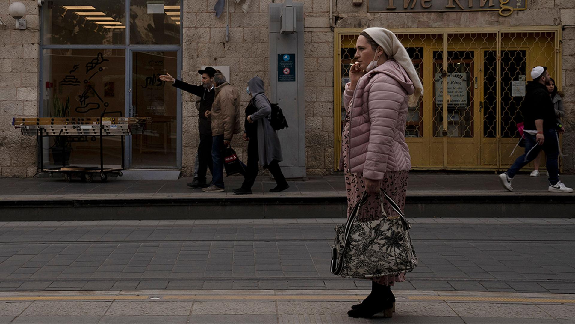 A woman speaks on her mobile phone while waiting for a light rail train, wearing a mask on her chin that she'll be required to pull over her nose and mouth on the train to help curb the spread of the coronavirus, in central Jerusalem.